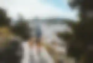 Vater und Kind gehen einen Weg entlang mit Blick auf eine weiße mediterrane Stadt in hügeliger Landschaft.
