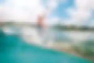 Person paddelt auf Surfboard im türkisfarbenen Meer vor tropischer Küste mit Palmen