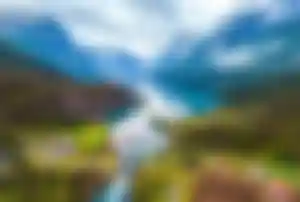 Weitwinkelaufnahme eines Fjords in Norwegen mit spiegelndem Wasser, steilen Bergen und kleinen Häusern in grüner Landschaft