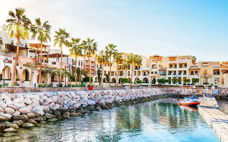 Uferpromenade in Aqaba mit Palmen, hellen Gebäuden und Boot am Steg.