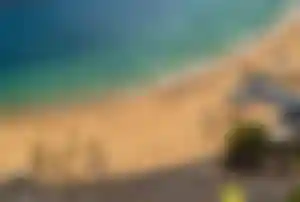 Goldener Sandstrand Playa de Las Teresitas mit Palmen, bunten Sonnenschirmen und türkisfarbenem Meer aus der Vogelperspektive.