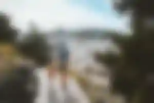 Erwachsene Person mit Rucksack geht gemeinsam mit einem Kind auf einem Wanderweg und blickt über eine weiße Ortschaft in hügeliger Landschaft.