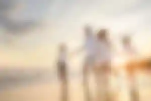 Alt-Tag: Vier Personen spazieren barfuß am Strand entlang der Wasserkante bei Sonnenuntergang
