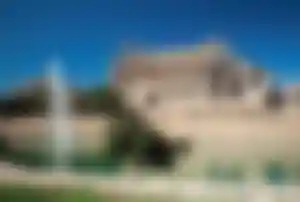 Kathedrale La Seu in Palma de Mallorca mit springendem Brunnen im Vordergrund und ruhigem Wasserbecken an der Stadtmauer unter blauem Himmel.