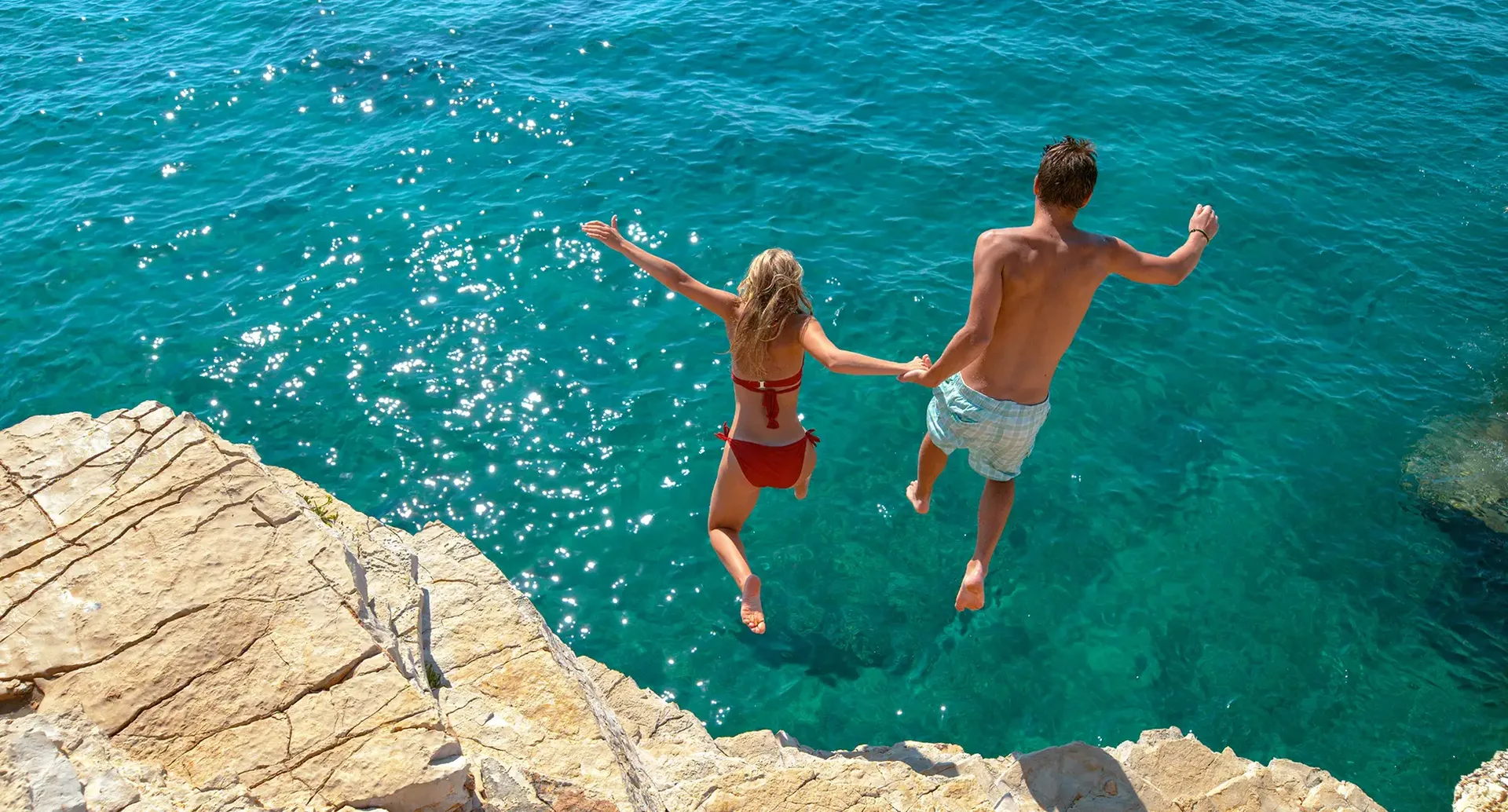 Zwei Personen springen von Felsen ins klare Meer in Kroatien